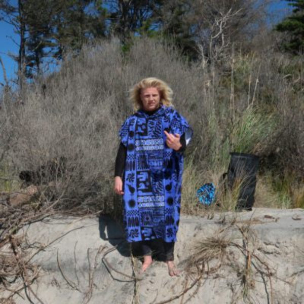 Person wearing a blue patterned poncho on a beach with dry grass and trees in the background