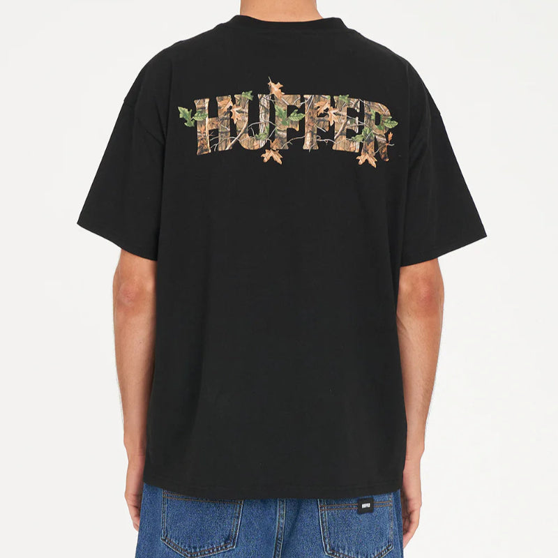 Person wearing a black Huffer t-shirt with camouflage text on the back, standing against a white background.