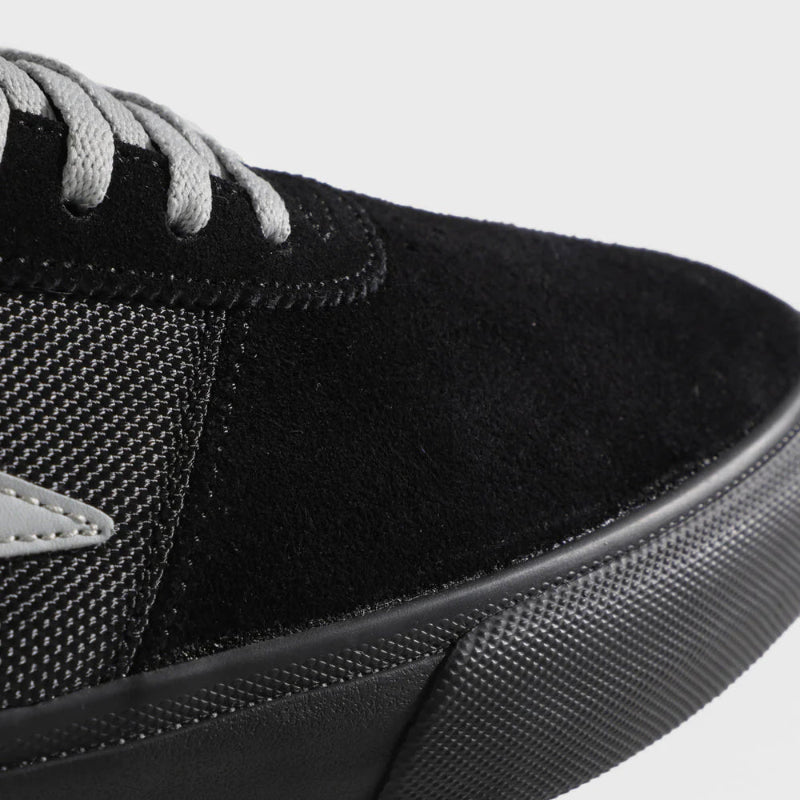 Close-up of a black sneaker with gray laces on a light gray background