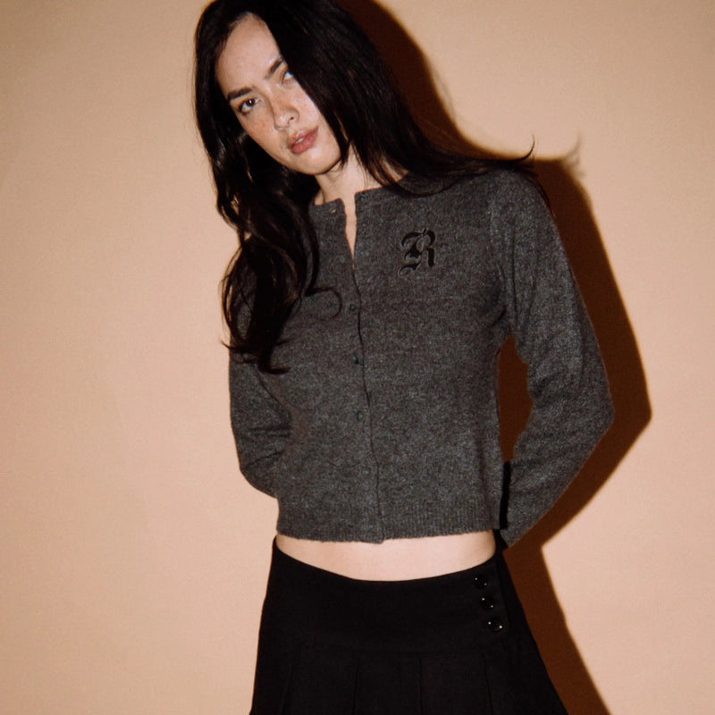 Woman wearing a dark gray cardigan with a logo on a beige background