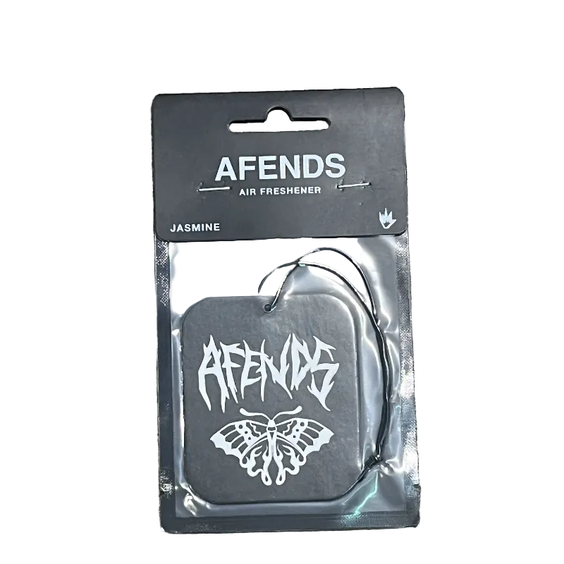 A packaged Afends Air Freshener in the Jasmine scent, featuring a square black air freshener tag with a white stylized logo and butterfly graphic, sealed in clear plastic on a black backing card, placed on a concrete surface.