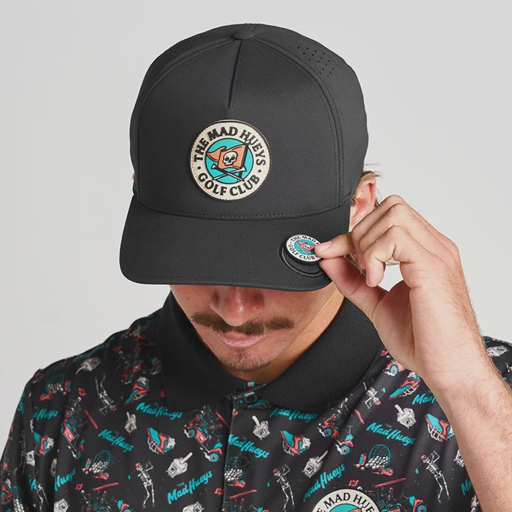 Person wearing a black cap with a logo and a matching patterned shirt on a gray background