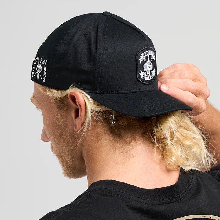 Person wearing a black cap with a logo and a black t-shirt with text, on a light gray background