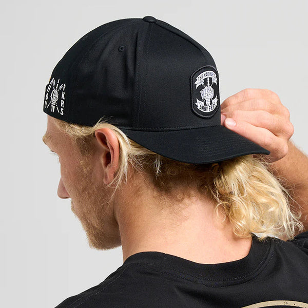 Person wearing a black cap with a logo and a black t-shirt with text, on a light gray background