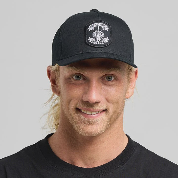 Man wearing a black cap and black t-shirt with a logo on a gray background