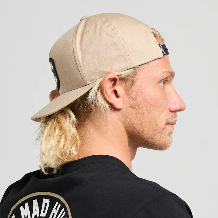 Person wearing a beige cap and black t-shirt with 'The Mad Hueys' logo on a gray background