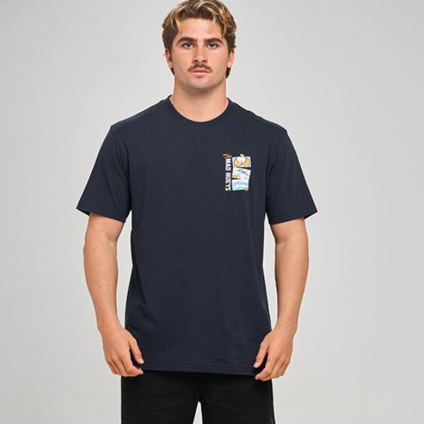 A man modeling a navy blue short-sleeve t-shirt with a small graphic on the left chest, paired with black athletic shorts, black socks, and black sneakers, against a light gray studio background.
