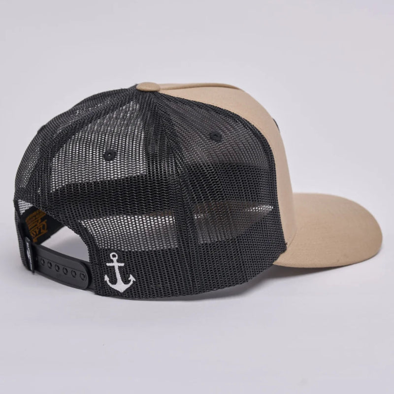 A beige and black trucker cap shown from the back, featuring a black mesh back, a beige curved brim, and a white anchor logo on the side.