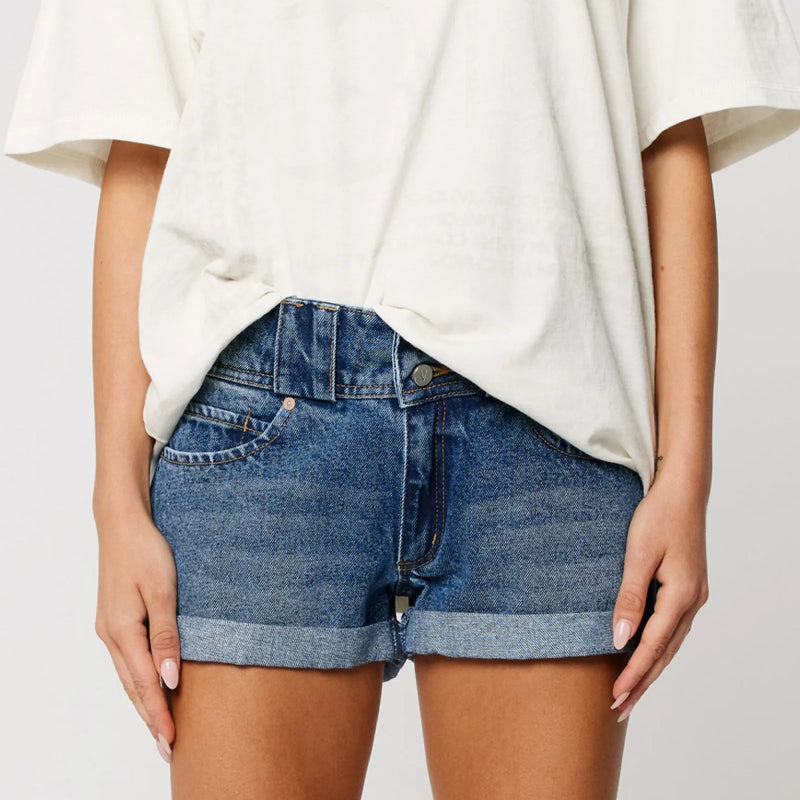 Person wearing blue denim shorts and a white oversized shirt on a plain background
