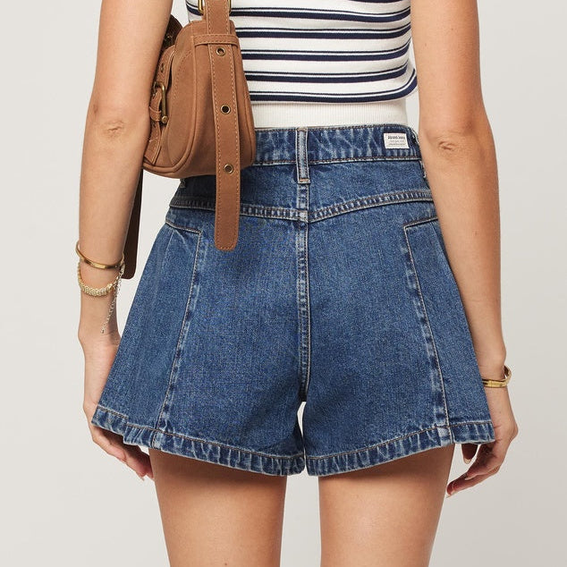 Person wearing blue denim shorts and a striped tank top with a brown bag on a light background