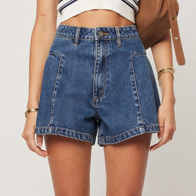 Person wearing a striped crop top and blue denim shorts with a brown bag on a light background