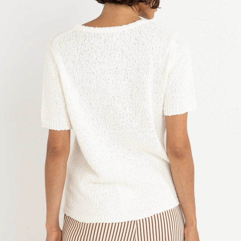 Woman wearing a white textured top and striped pants on a plain background