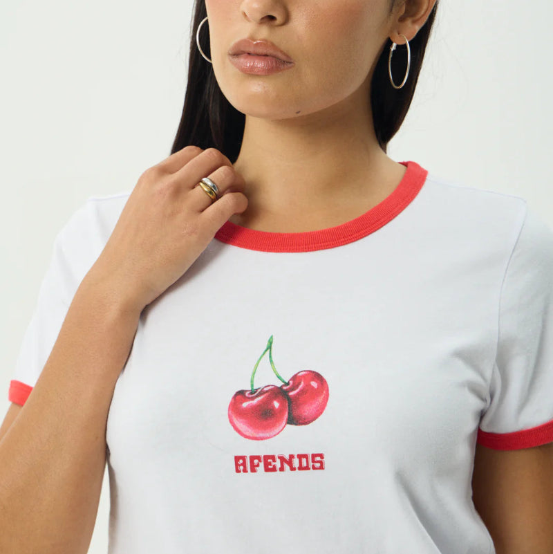 Woman wearing a white t-shirt with red trim and cherry design, standing against a plain background.