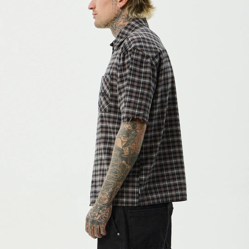 Person wearing a plaid shirt and black pants on a white background