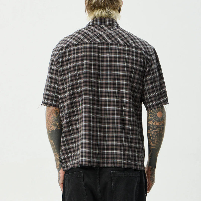 Person wearing a plaid shirt with tattoos on arms against a white background