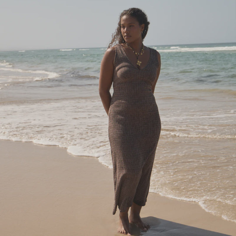Woman in a long brown dress standing on a beach with ocean waves in the background