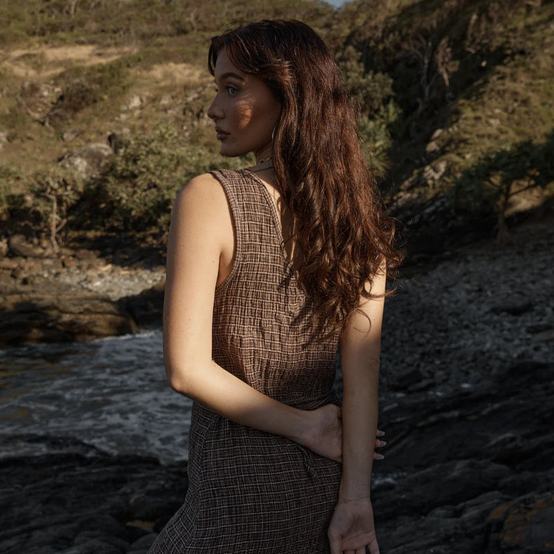 Woman in a brown dress standing by a body of water with trees in the background