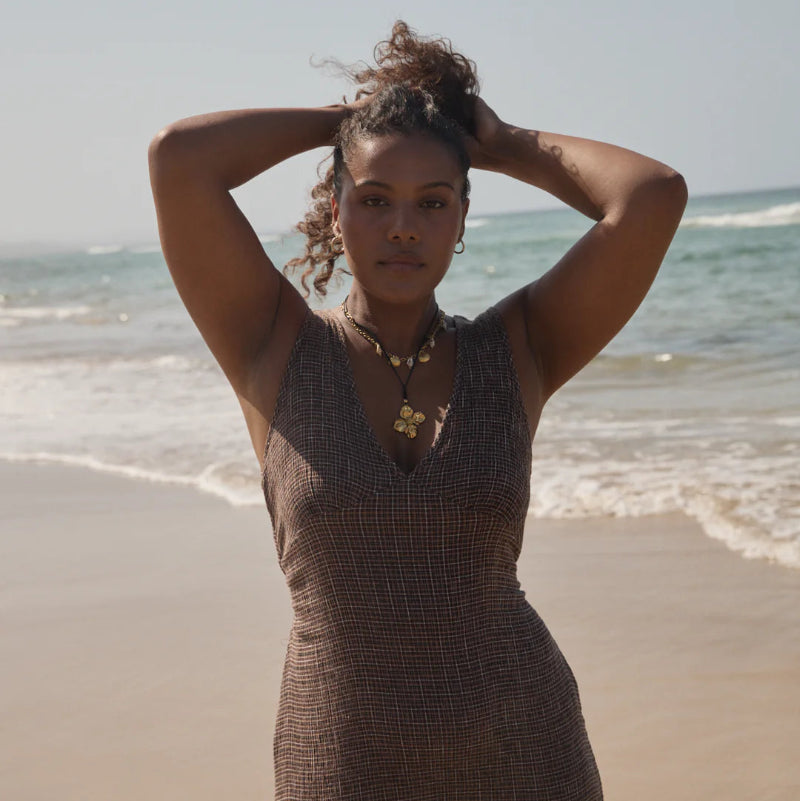 Woman in a brown dress standing on a beach with ocean waves in the background