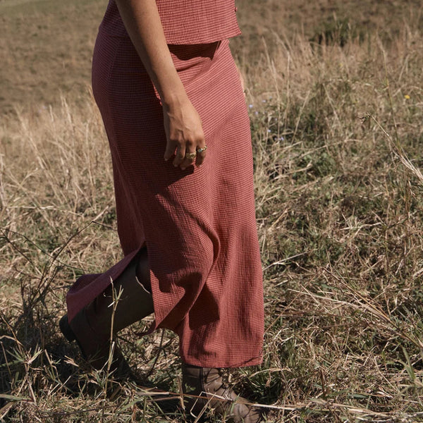 A person wearing a rust-colored textured two-piece outfit consisting of a sleeveless crop top and a long skirt, walking through a dry grassy field.