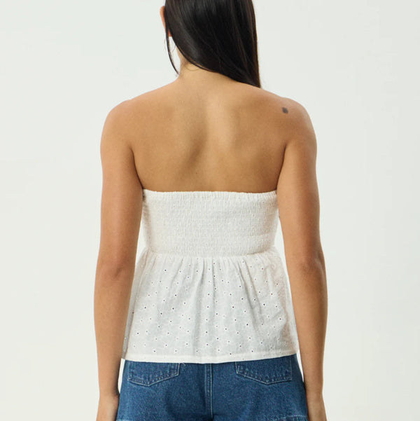 Woman wearing a white strapless top and blue denim shorts on a plain background