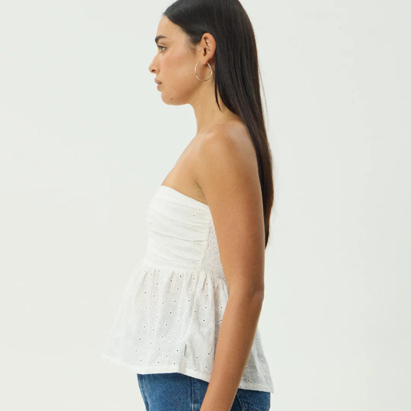 Woman wearing a white strapless top and blue denim shorts on a plain background