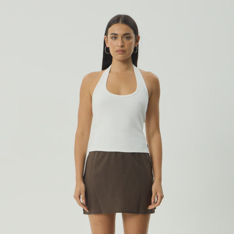 Woman wearing a white halter top and brown skirt on a gray background