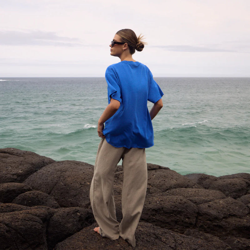 Person wearing a blue shirt and beige pants standing on rocky terrain by the ocean.