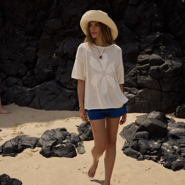 Woman in a white top and blue shorts standing on a rocky beach.