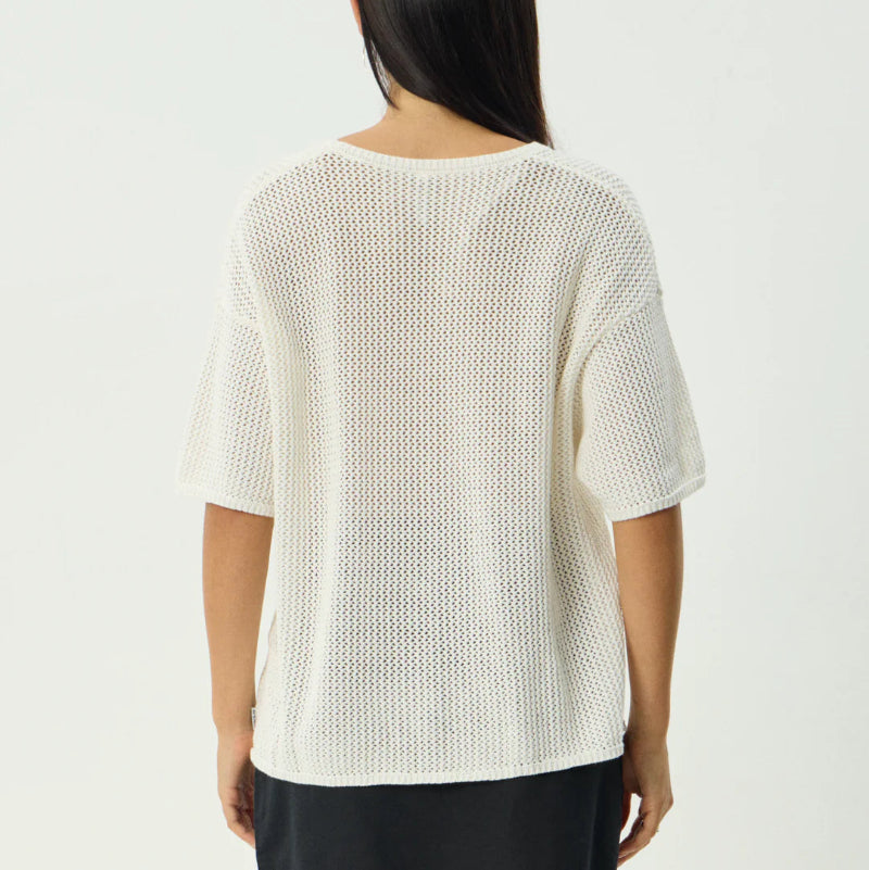 Woman wearing a white textured top and black shorts on a plain background