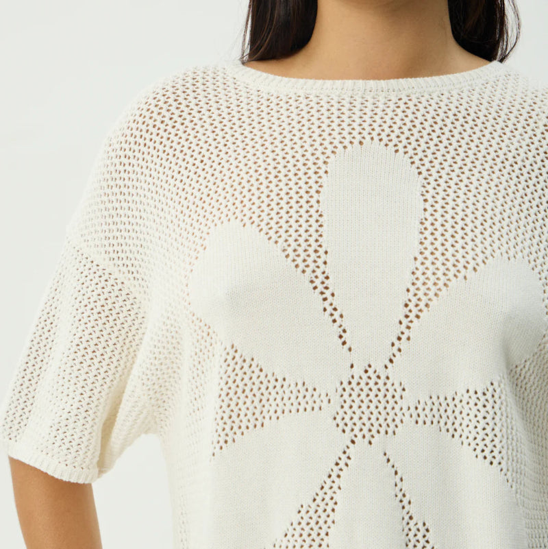 Woman wearing a white knit top with a leaf pattern on a plain background