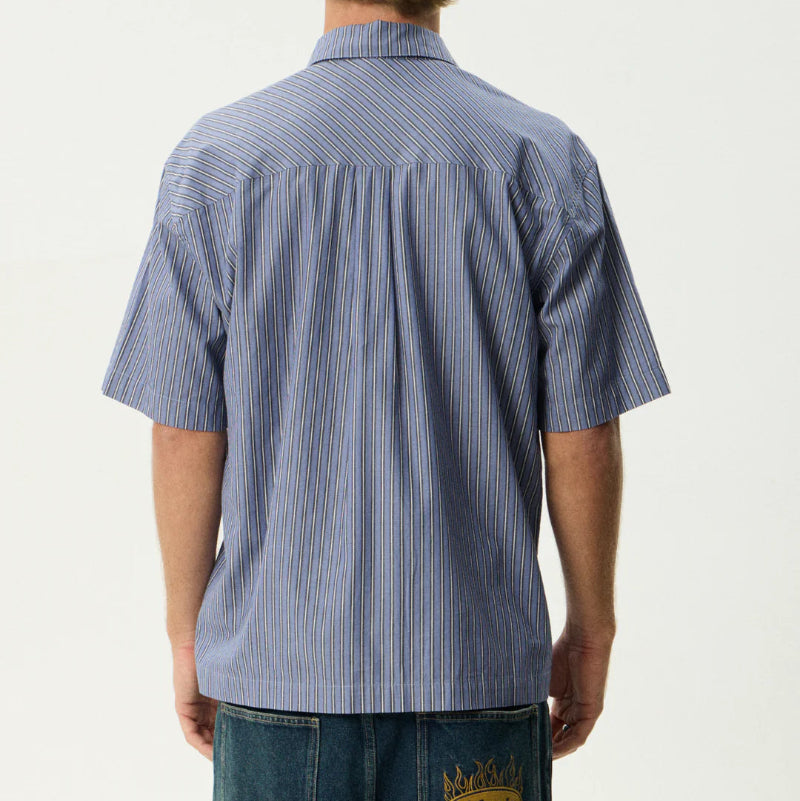 Person wearing a blue striped shirt and jeans with a visible brand logo on a white background