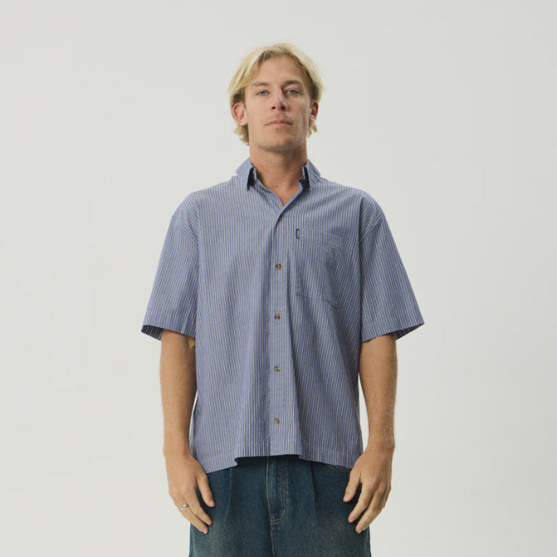 Man wearing a short-sleeve button-up shirt and denim shorts on a plain background