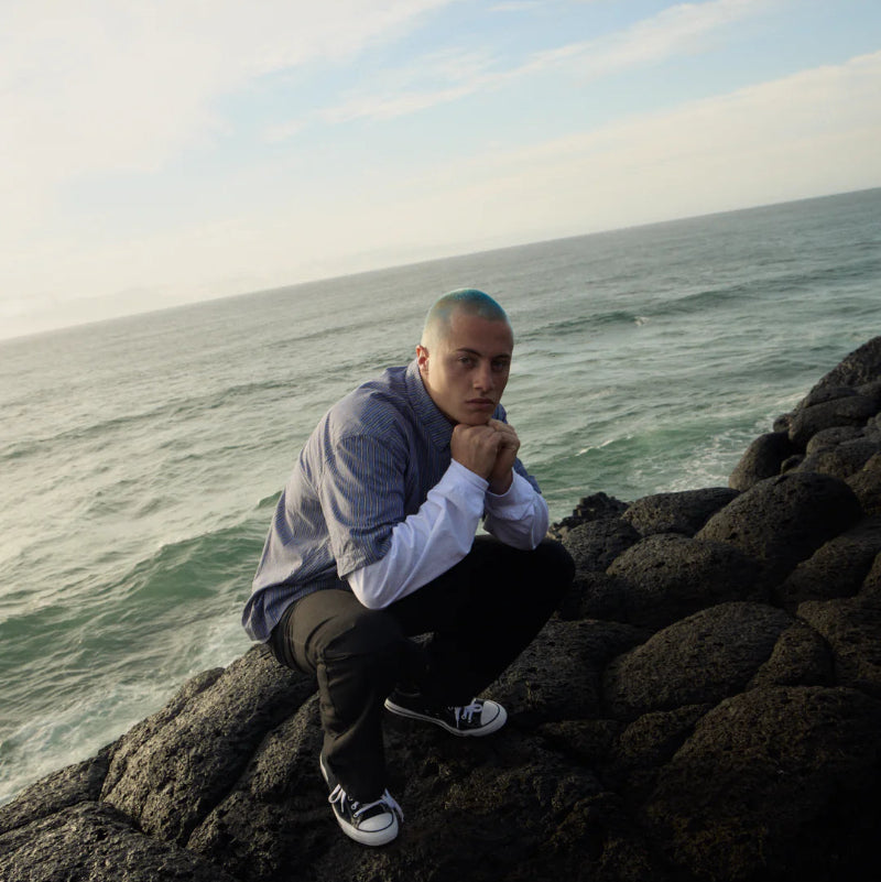 Person sitting on rocks by the ocean with a blue sky.