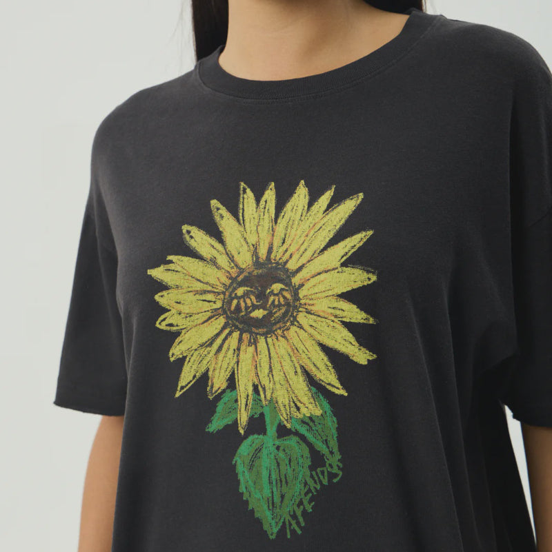 Person wearing a black t-shirt with a yellow sunflower design on a plain background
