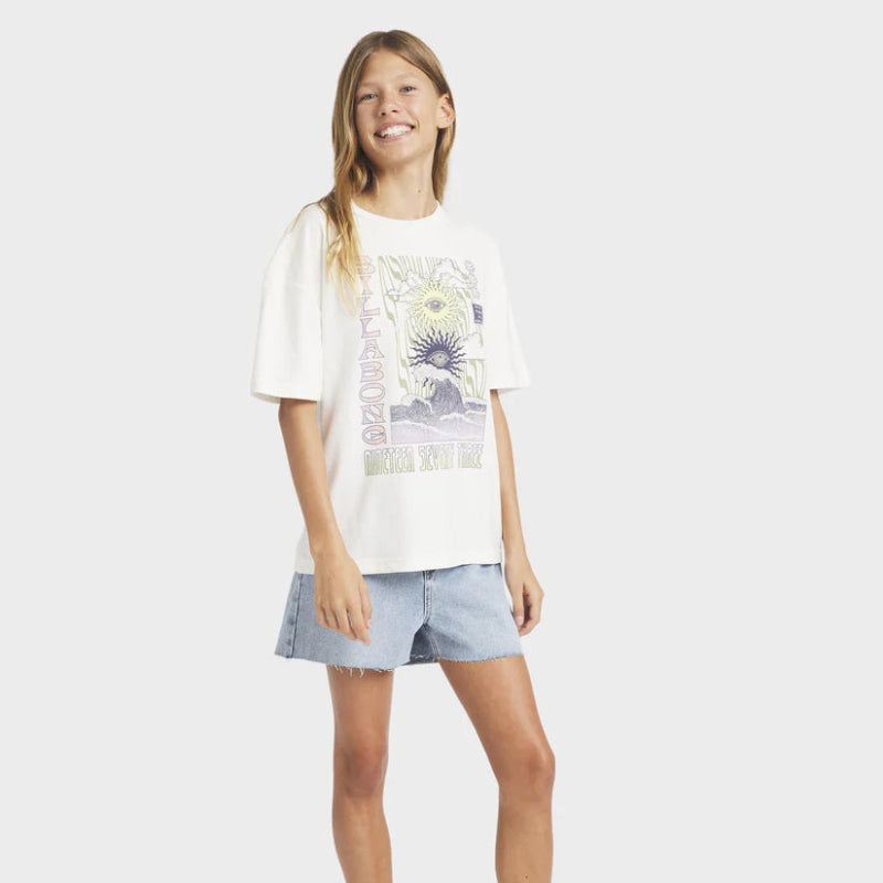 Young girl wearing a white t-shirt with a graphic design and denim shorts on a plain background