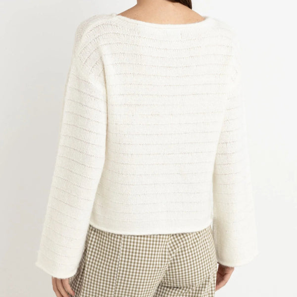 Woman wearing a white textured sweater and plaid pants on a plain background
