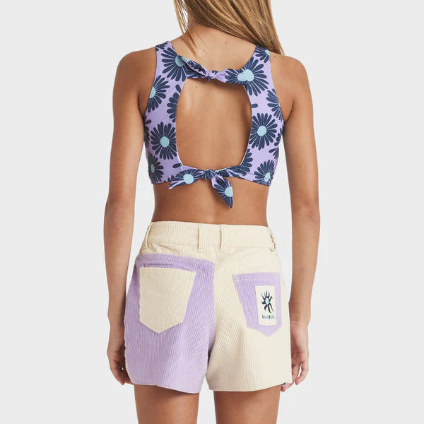 Woman wearing a purple floral crop top and beige shorts with pocket designs on a white background