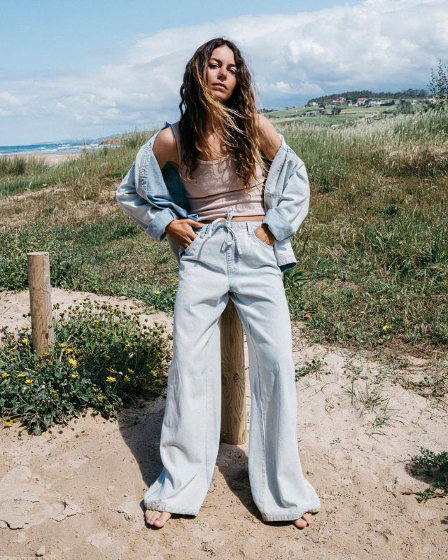 Woman standing on a sandy path with grass and ocean in the background