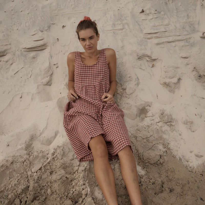 Person wearing a red checkered dress sitting on a textured stone surface.