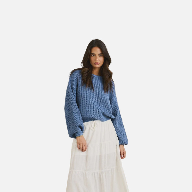 Woman wearing a blue sweater and white skirt against a beige background