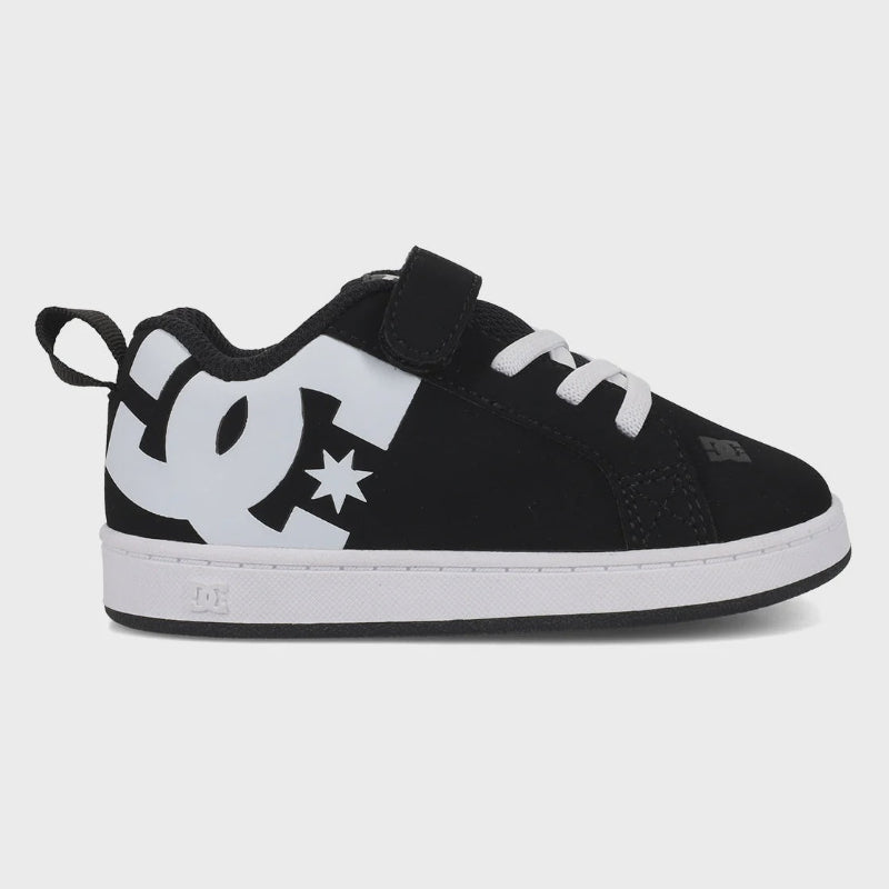 A DC Shoes toddler sneaker in black and white, featuring a hook-and-loop strap closure, white laces, and a large white DC logo on the side with a star detail, shown against a light gray background.