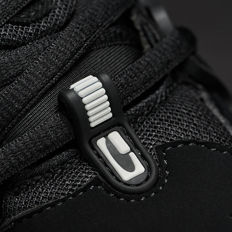 Close-up of a black sneaker with a distinctive white and black plastic hook-and-loop strap closure on the side.