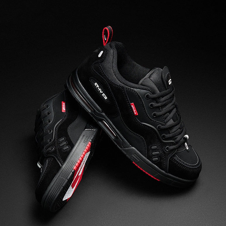 A pair of black low-top athletic sneakers with red and white accents, displayed on a dark gray studio background.