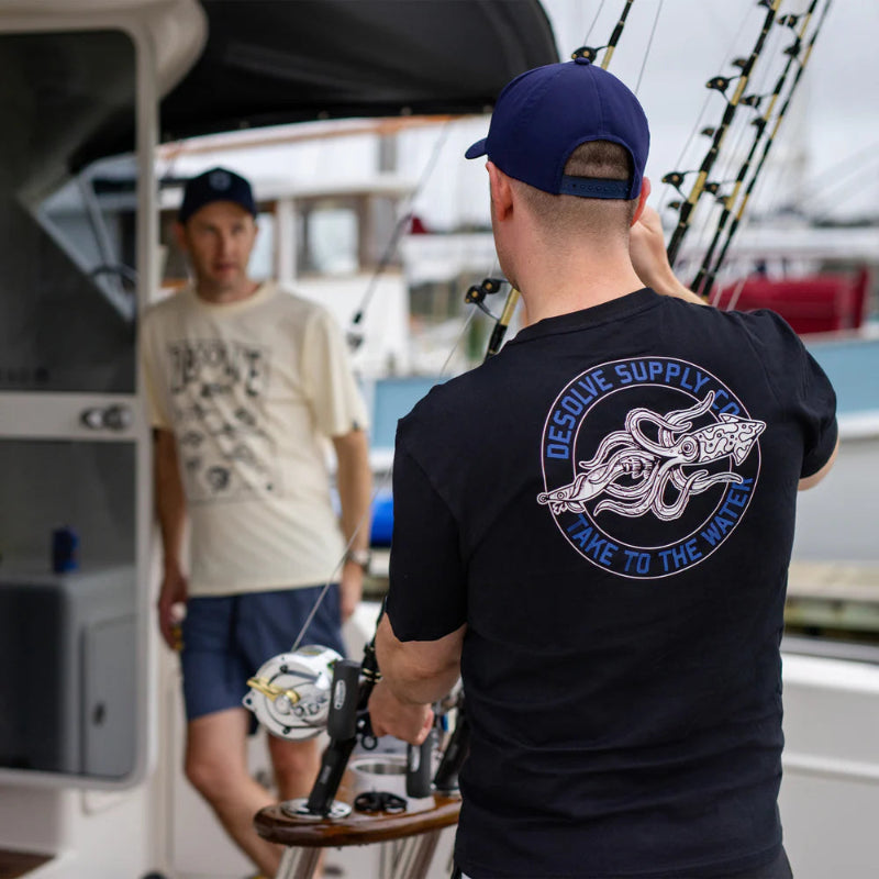 Man on a boat wearing a black t-shirt with a logo and text, another person in the background.