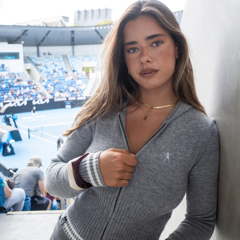 Woman in a gray zip-up sweater standing in an outdoor setting with a blurred background