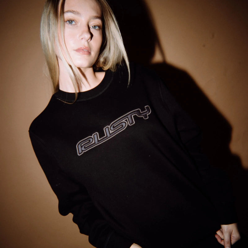 Person wearing a black sweatshirt with 'Rusty' logo against a brown background