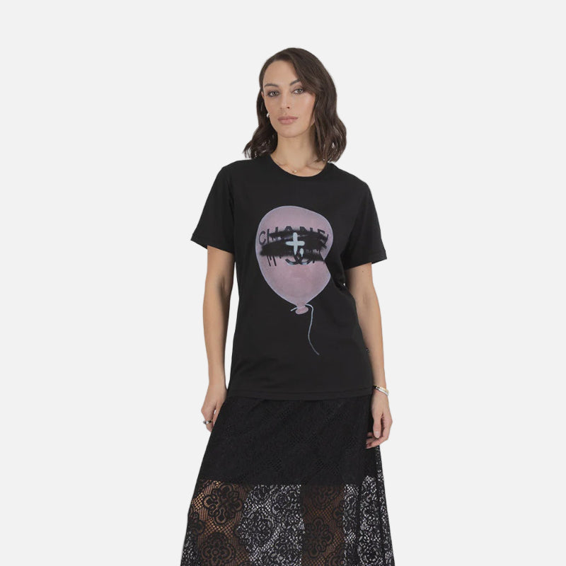 Woman wearing a black t-shirt with a graphic design and a long black skirt with patterns on a gray background