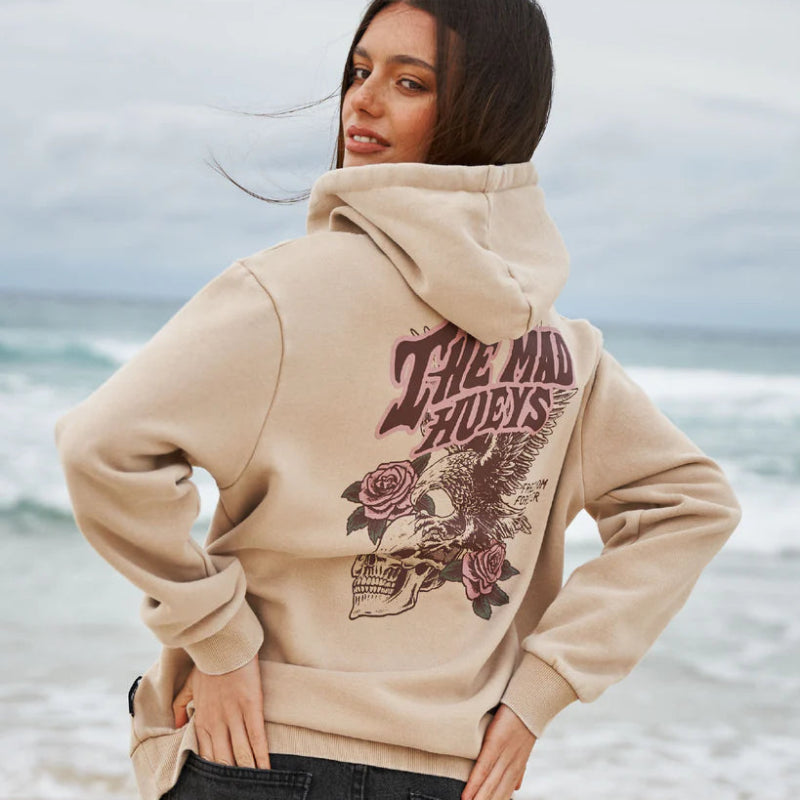 Person wearing a beige hoodie with graphic design on a beach