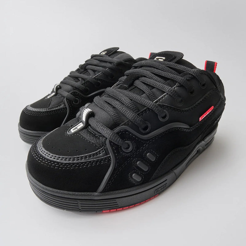 A pair of black skate-style sneakers with gray laces and small red accents on the side and heel, photographed on a light gray studio background.