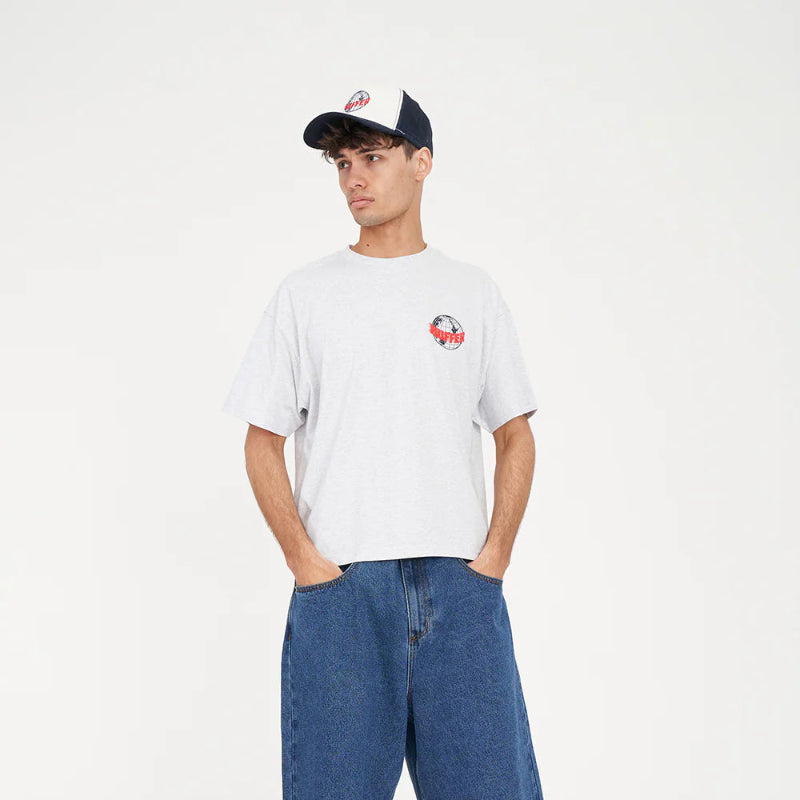 Person wearing a white t-shirt with a logo, blue shorts, black sneakers, and a cap on a white background